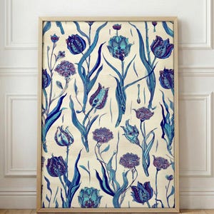 Op de afbeelding: Een ingelijste bloemenprint met een herhalend patroon van blauwe en paarse tulpen en bladeren op een crèmekleurige achtergrond. Het kunstwerk wordt weergegeven in een lichtgekleurde houten lijst en leunt tegen een witte muur.