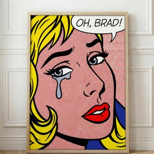 May include: Pop art print featuring a crying woman with blonde hair, red lips, and a tear. The speech bubble says "OH, BRAD!". The artwork is framed in a light wood frame and has a red and white dotted background.