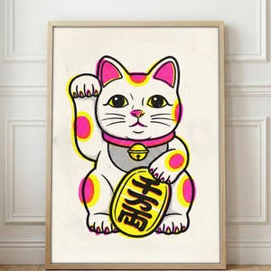 May include: A framed print featuring a stylized Maneki-neko cat illustration. The cat is white with pink and yellow accents, a pink collar, and a gold coin. The Japanese text on the coin is visible. The artwork is set against a white background.