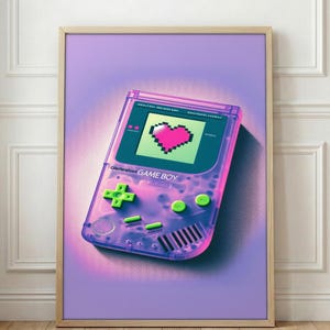 Puede incluir: Impresión enmarcada que presenta una Game Boy de estilo retro. La consola portátil está representada en rosa transparente con botones verdes y un corazón pixelado en la pantalla. Las palabras "GAME BOY" son visibles en el dispositivo.