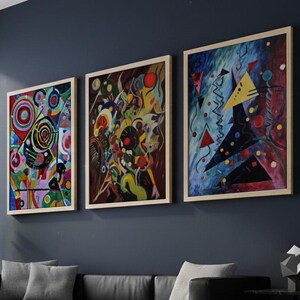 May include: Three framed abstract art prints hang above a black leather sofa. The artwork features colorful geometric shapes and patterns in red, blue, yellow, and green. A potted plant and a side table with a geometric sculpture complete the room.