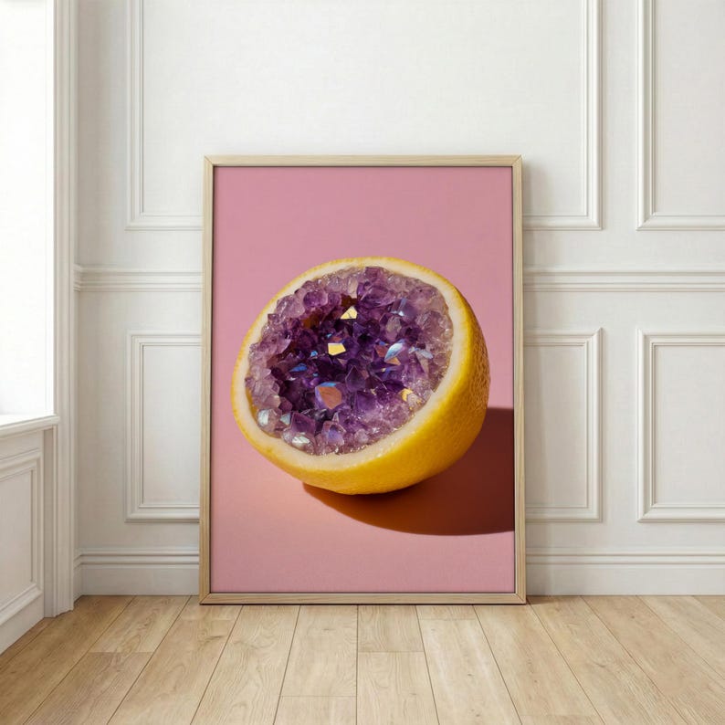 May include: A framed print featuring a halved lemon with a vibrant purple amethyst geode center. The lemon is yellow, set against a pink background. The artwork is displayed in a light-colored wooden frame, creating a striking contrast.