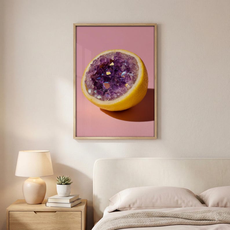 May include: A framed art print featuring a halved lemon with a geode interior. The geode is filled with sparkling purple crystals, set against a pink background. The lemon is yellow, and the frame is a light wood color.