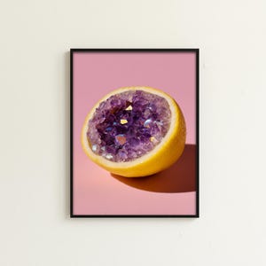 May include: A framed print featuring a halved lemon with a vibrant purple geode center. The lemon's yellow rind contrasts with the geode's sparkling crystals. The artwork is set against a pink background, creating a striking visual.
