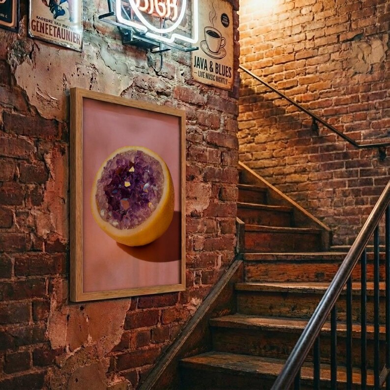 May include: A framed print featuring a cross-section of a yellow citrus fruit with a purple crystal geode center. The artwork is displayed on a brick wall, with a staircase and vintage signs in the background.