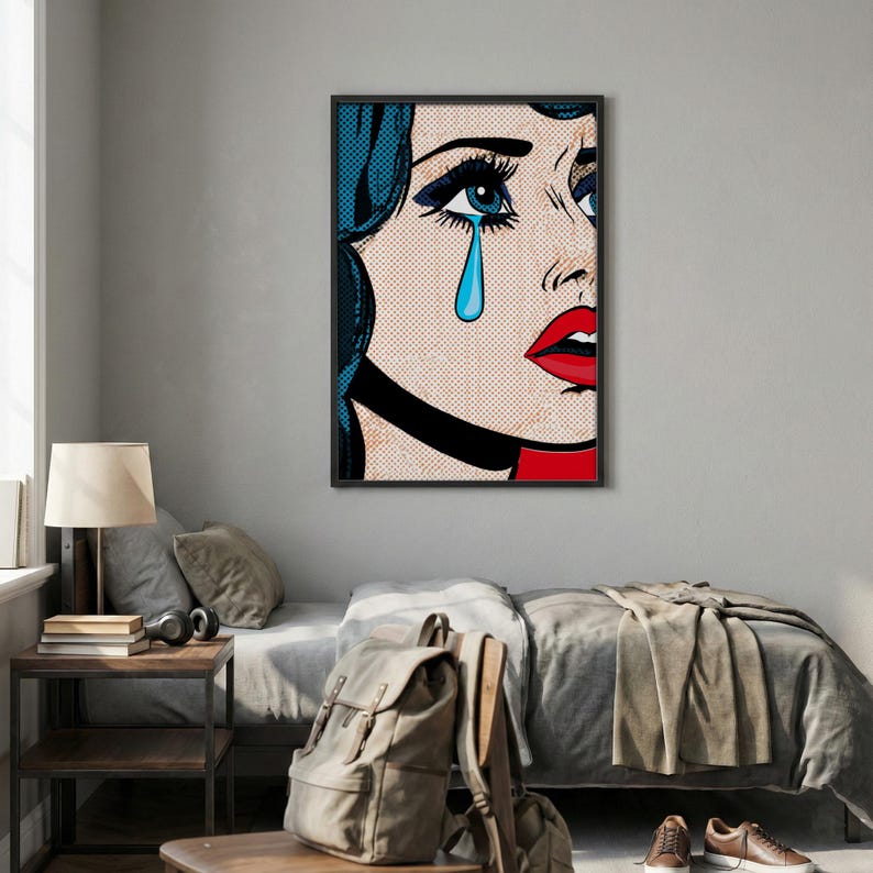 May include: Pop art style framed print featuring a close-up of a crying woman. The artwork uses bold colors, including blue hair, red lips, and a tear. The image is framed in a black border and is displayed in a bedroom setting.