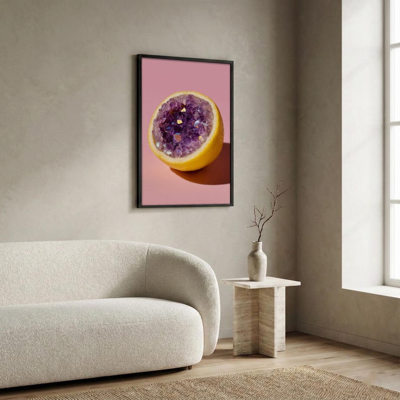 May include: A framed print featuring a halved lemon with a geode center. The geode is filled with purple crystals and gold flecks, set against a pink background. The lemon's yellow rind contrasts with the geode's colors.