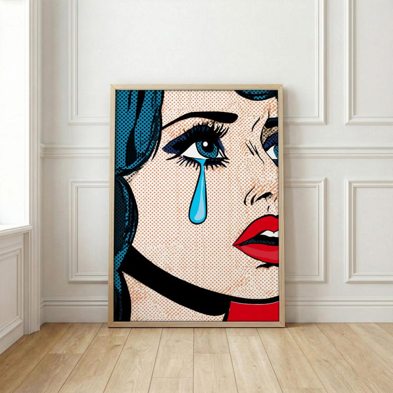 May include: Pop art print of a woman with blue hair and a tear falling from her eye. The artwork features bold lines, a red lip, and a black choker. The background is a dotted pattern, and the print is framed.