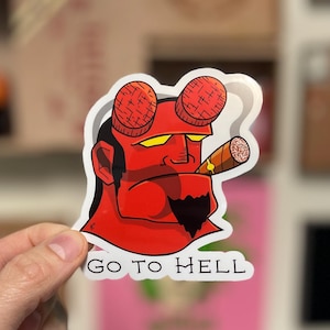 Puede incluir: Una pegatina roja con un personaje de dibujos animados con piel roja, ojos amarillos y un cigarro. La pegatina tiene el texto blanco "GO TO HELL".