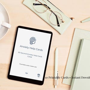 Może przedstawiać: Tablet cyfrowy wyświetla "Anxiety Help Cards" z tekstem "60-Second Anxiety Help Cards" i "10 printable cards + instant calm". Obraz zawiera filiżankę kawy, okulary, długopis i notatnik na jasnej drewnianej powierzchni.