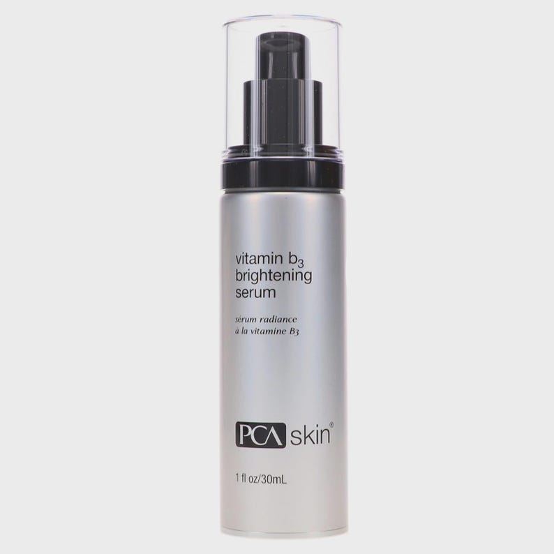 May include: A silver-colored bottle of PCA Skin Vitamin B3 Brightening Serum. The bottle has a black pump and a clear plastic cap. The label includes the text "vitamin b3 brightening serum" and "serum radiance &agrave; la vitamine B3". The bottle contains 1 fl oz / 30mL.