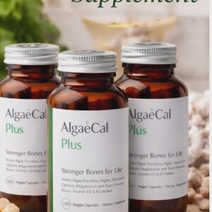 May include: Three amber glass bottles of AlgaeCal Plus plant-based bone health supplement. Each bottle has a white label with green text. The bottles are on a wooden cutting board, with the words "Plant-Based Bone Health Supplement" at the top.