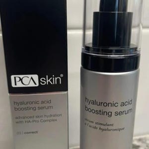 May include: A silver PCA skin hyaluronic acid boosting serum bottle with a black pump and clear cap, next to a black box with the same branding. The box and bottle both feature the product name and details.