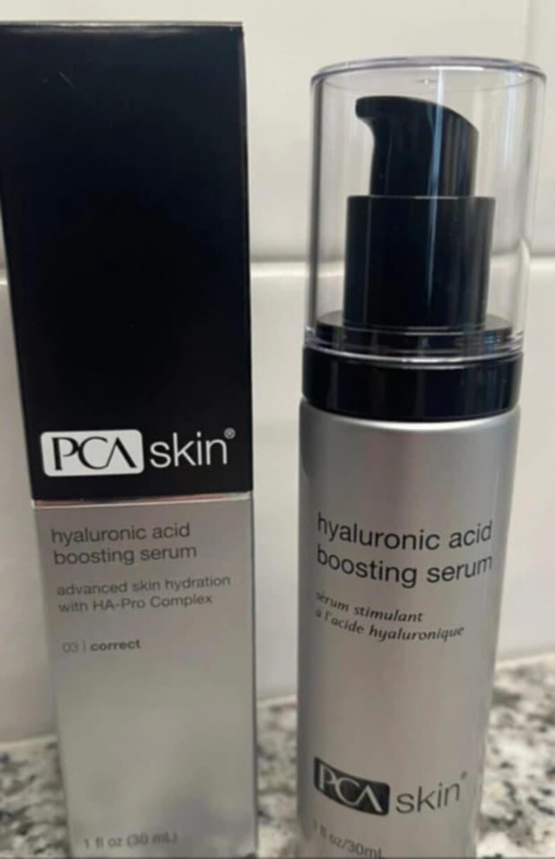 May include: A silver PCA skin hyaluronic acid boosting serum bottle with a black pump and clear cap, next to a black box with the same branding. The box and bottle both feature the product name and details.