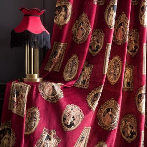May include: Burgundy velvet curtains with a repeating pattern of framed portraits. A red lampshade with black fringe sits on a table. The curtains add a touch of vintage elegance to any room.