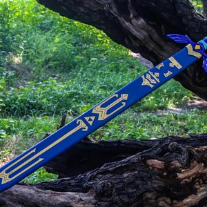 May include: A blue and gold decorative sword, featuring intricate designs and a stylized hilt. The blade is a vibrant blue with gold accents, and the hilt has a detailed design. The sword is resting on a tree trunk, with greenery in the background.