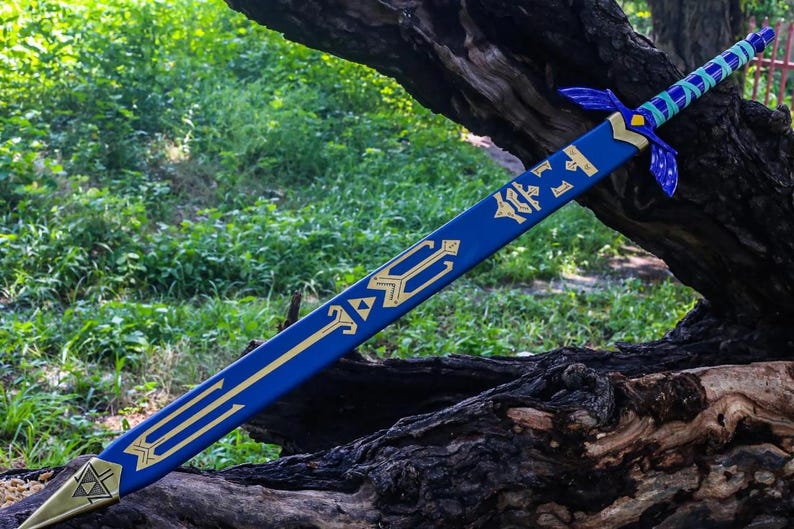 May include: A blue and gold decorative sword, featuring intricate designs and a stylized hilt. The blade is a vibrant blue with gold accents, and the hilt has a detailed design. The sword is resting on a tree trunk, with greenery in the background.