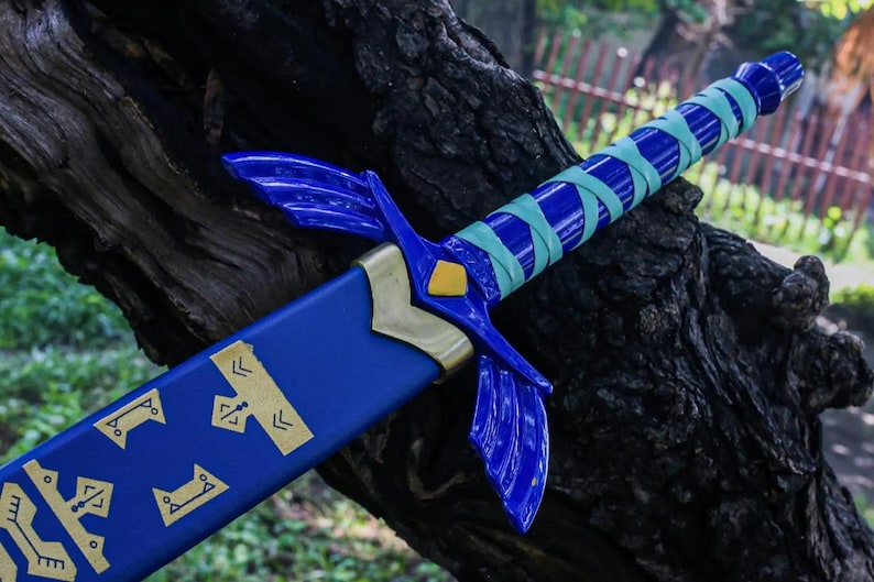 May include: A blue and gold fantasy sword with a wrapped handle. The sword features a blue blade with gold accents and a crossguard with wing-like designs. The handle is wrapped in blue and teal tape. The sword is resting on a tree trunk.