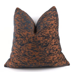 Op de afbeelding: Een vierkant decoratief kussen met een textuurpatroon. Het kussen heeft een bruine achtergrond met een donkerblauw, gespikkeld ontwerp. Het kussen is gemaakt van een zachte stof en is ontworpen voor woondecoratie.