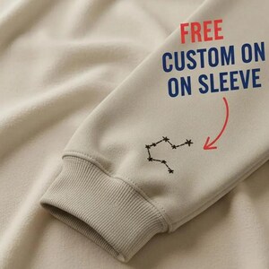 Pode incluir: Uma caneca de cer&acirc;mica branca com uma al&ccedil;a preta e o texto "But First, Coffee" em negrito preto. A caneca est&aacute; sobre um fundo desfocado, sugerindo um ambiente acolhedor.