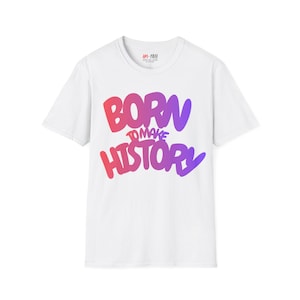 Puede incluir: Una camiseta blanca de manga corta con el texto BORN TO MAKE HISTORY en un degradado de rojo, rosa y morado. El nombre de la marca AM-FREE está impreso en negro en la etiqueta interior del cuello de esta prenda de algodón.