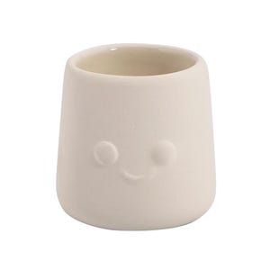 May include: A small, off-white ceramic cup with a smiling face design. The cup has a rounded bottom and a wide opening. The face is made up of two small circles for eyes and a curved line for a smile.