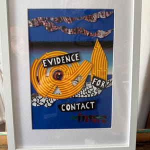 Op de afbeelding: Ingelijst kunstwerk met een collage-ontwerp. Het kunstwerk bevat de woorden "EVIDENCE FOR CONTACT" in vette tekst. De collage bevat gele, rode en blauwe elementen, met een centraal oogmotief. De lijst is wit.