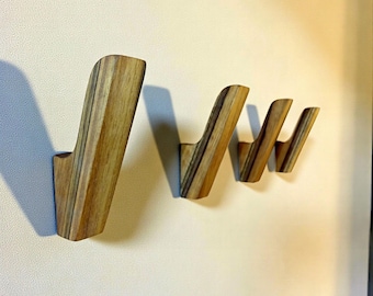 May include: Set of four wooden wall hooks with a natural wood grain finish. The hooks are mounted on a light-colored wall. Each hook has a unique angled design, perfect for hanging coats, bags, or other items. The hooks are approximately 6 inches in height.