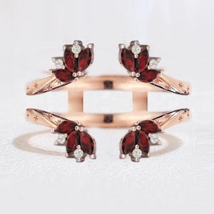 Può includere: Protezione per anello in oro rosa con quattro gruppi di pietre rosse e piccole pietre bianche. La protezione per anello ha un design floreale, su sfondo bianco.