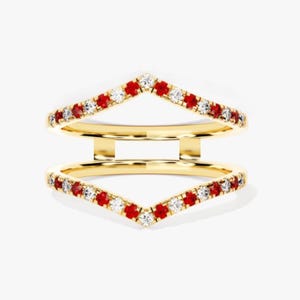 Puede incluir: Un protector de anillo dorado con un diseño en forma de V. El anillo está adornado con gemas rojas y blancas alternas. El protector de anillo está diseñado para usarse con otro anillo.