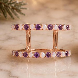 May include: A rose gold double band ring featuring two parallel rows connected by vertical bars. Each band is set with alternating round purple amethyst stones and white opalescent cabochons, creating a symmetrical and structured jewelry piece.
