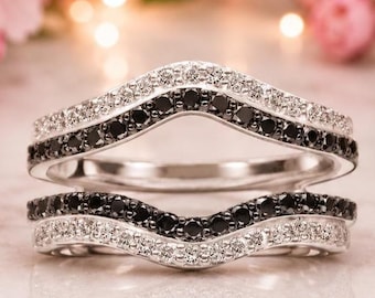 May include: A silver ring guard featuring a chevron shape with two rows of pavé-set stones. The outer bands are lined with clear white stones, while the inner bands are set with black stones, creating a layered, contrasting metallic design.