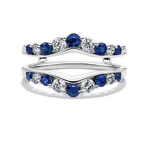 Puede incluir: Un protector de anillo plateado con un diseño curvo, engastado con piedras preciosas azules y claras redondas alternas. El protector de anillo está diseñado para colocarse junto a un anillo, realzando su apariencia.