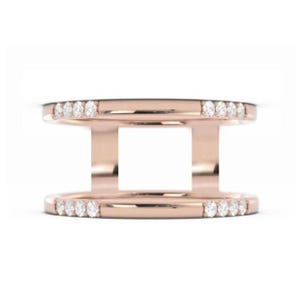 Puede incluir: Anillo de oro rosa con un diseño de doble banda. Las bandas superior e inferior están adornadas con pequeñas piedras preciosas transparentes. El anillo tiene un estilo moderno y calado, con un espacio cuadrado en el centro.