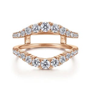 May include: Rose gold ring with a double band design. The top and bottom bands are adorned with a series of round, clear gemstones. The ring has a curved shape, with the gemstones set in a channel setting.