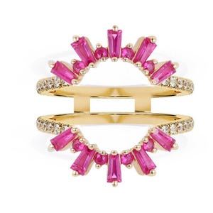 May include: A gold-colored ring with a double band design. The top and bottom bands are encrusted with small, clear stones. The ring features a sunburst design of pink rectangular and round stones.