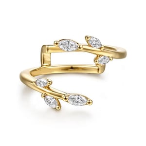 Puede incluir: Un anillo dorado con un diseño de hojas. El anillo presenta varias piedras preciosas claras con corte marquesa. El anillo tiene un diseño único y abierto, con una banda que rodea el dedo y una pieza separada encima.