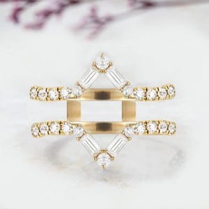 Puede incluir: Un anillo de oro con una banda con incrustaciones de diamantes y un diseño geométrico. El anillo presenta una disposición central de diamantes con piedras de talla baguette y diamantes redondos más pequeños, creando un efecto brillante.