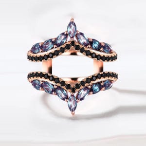 Puede incluir: Anillo de oro rosa con dos bandas. Cada banda presenta una fila de pequeñas piedras negras y una fila de piedras ovaladas de color azul-púrpura. El anillo tiene un diseño abierto único.