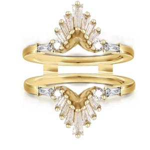 Puede incluir: Un protector de anillo dorado con un diseño de doble banda. El anillo presenta una parte superior en forma de V adornada con múltiples piedras preciosas claras de talla baguette y redonda. Las piedras están dispuestas en forma de abanico.