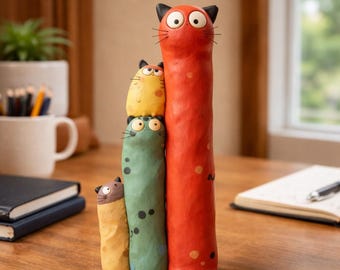 May include: A vertical sculpture featuring four stacked, stylized cat figures. The tallest cat is bright red, followed by a green cat, a yellow cat, and a small brown cat at the base. Each cat has wide, circular eyes, black ears, and thin whiskers.