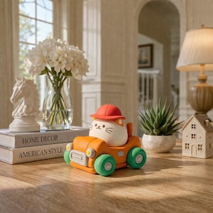 May include: An orange toy car with green wheels carries a white cat wearing a red hat. The cat has black whiskers and a smiling face. The car is on a wooden surface, with a white chess piece and a vase of white flowers in the background.