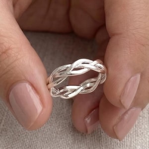 May include: A polished silver ring featuring a multi-strand braided design. The band is constructed from several thin, interconnected metallic wires that weave together to form a continuous, circular pattern with a smooth, reflective finish.