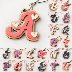 Può includere: Una collezione di 26 design di lettere dell'alfabeto, ognuno con una combinazione di colori unica e dettagli a forma di cuore. Le lettere sono a strati, con una base in legno e strati superiori colorati. L'immagine include il testo "26 DISEGNI" e "DOWNLOAD DIGITALE".