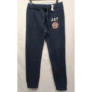 May include: Navy blue sweatpants with a drawstring waist and side pockets. The pants feature the text "A&F" in white block letters above a circular patch with "92" and "Abercrombie & Fitch Dept of Athl" in red and white.