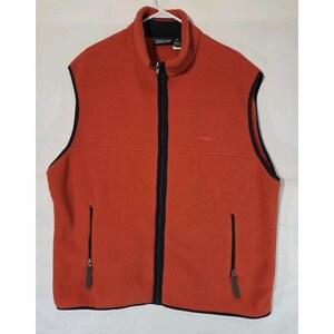 Peut inclure: Un gilet en polaire sans manches de couleur orange brûlé vif, doté d'une fermeture éclair noire sur toute la longueur, d'un col montant et de deux poches verticales zippées à la taille. Les emmanchures et l'ourlet sont bordés de noir.