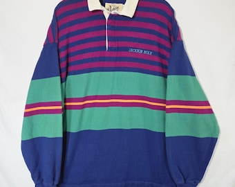 Könnte beinhalten: Ein langärmeliges Rugby-Shirt mit horizontalen Streifen in Lila, Grün und Blau sowie dünnen orangefarbenen Akzenten. Das Shirt hat einen weißen Kragen, eine Knopfleiste und den Schriftzug JACKSON HOLE in Blau auf der Brust gestickt.