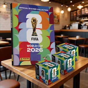 Könnte beinhalten: Ein Sammelalbum für FIFA World Cup 2026-Aufkleber und Stickerboxen. Das Album zeigt die FIFA World Cup-Trophäe auf einem farbenfrohen geometrischen Hintergrund. Die Boxen sind würfelförmig und tragen das FIFA World Cup 2026-Logo.