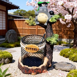 Könnte beinhalten: Ein dekorativer Stifthalter mit einer Totoro-Figur auf einem Ast. Der Stifthalter ist ein schwarzer Drahtgitterkorb mit Holzsockel. Die Abmessungen betragen 13,5 cm x 12 cm x 24 cm.