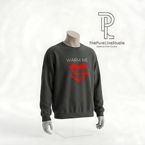 May include: Dark gray sweatshirt with the text "WARM ME" above a red heart graphic with hugging arms. The PureLineStudio logo is in the upper right corner. The sweatshirt is displayed on a mannequin.